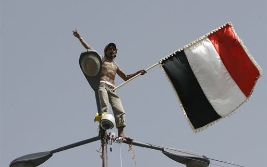 Ємен, Сана. Єменський антиурядовий демонстрант розмахує прапором, стоячи на ліхтарі під час демонстрації з вимогою відставки президента Ємену Алі Абдалли Салеха. / © AFP