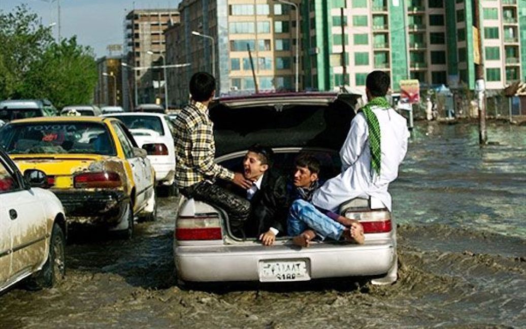 Афганістан, Кабул. Афганські молодики сидять в багажнику автомобіля, доки вони їдуть вулицею Кабула, яку затопило в результаті раптової зливи. / © AFP