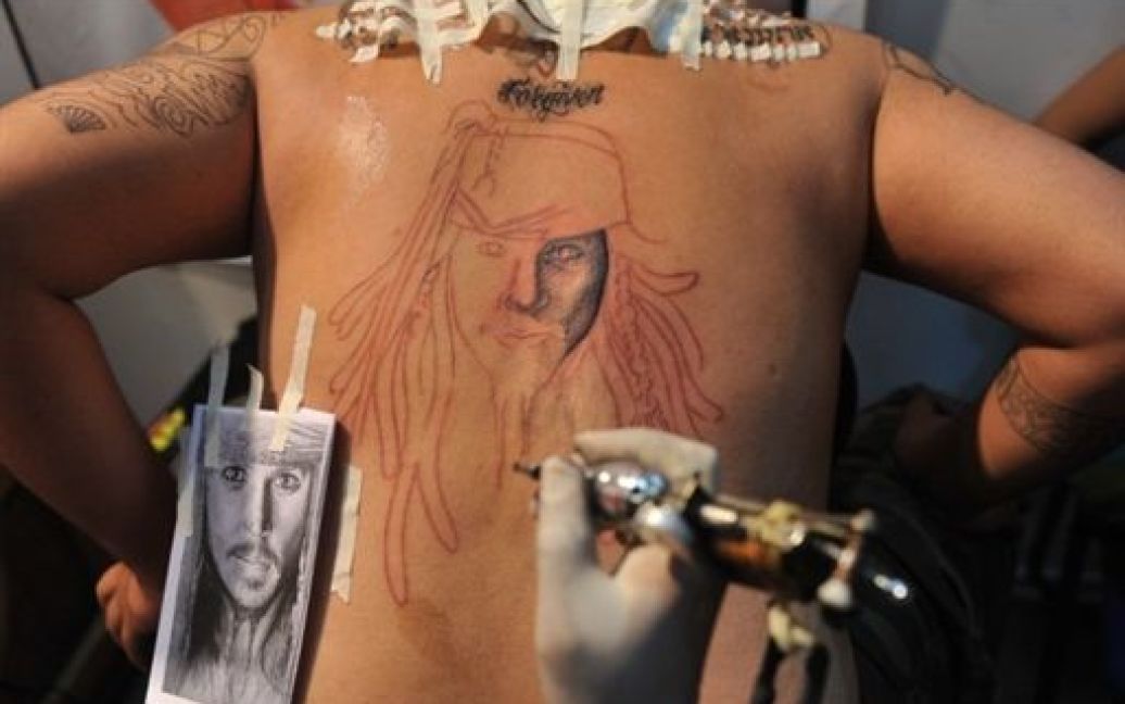 Індія, Мумбаї. Майстер робить татуювання головного героя фільму "Пірати Карибського моря" капітана Джека Горобця, якого грає Джонні Депп, на спині людини під час проведення тату-конвенції в Мумбаї. / © AFP