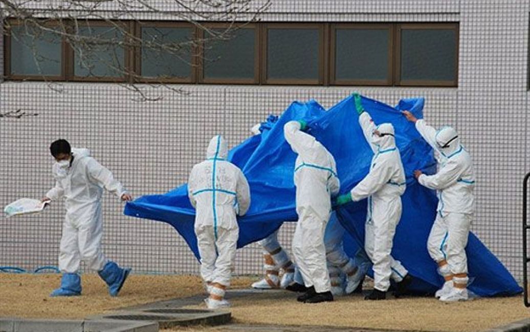 Японія, Фукусіма. Офіцери японських сил самооборони у костюмах радіаційного захисту захищають людей, які отримали опромінення під час ліквідації аварії на АЕС "Фукусіма-1". / © AFP