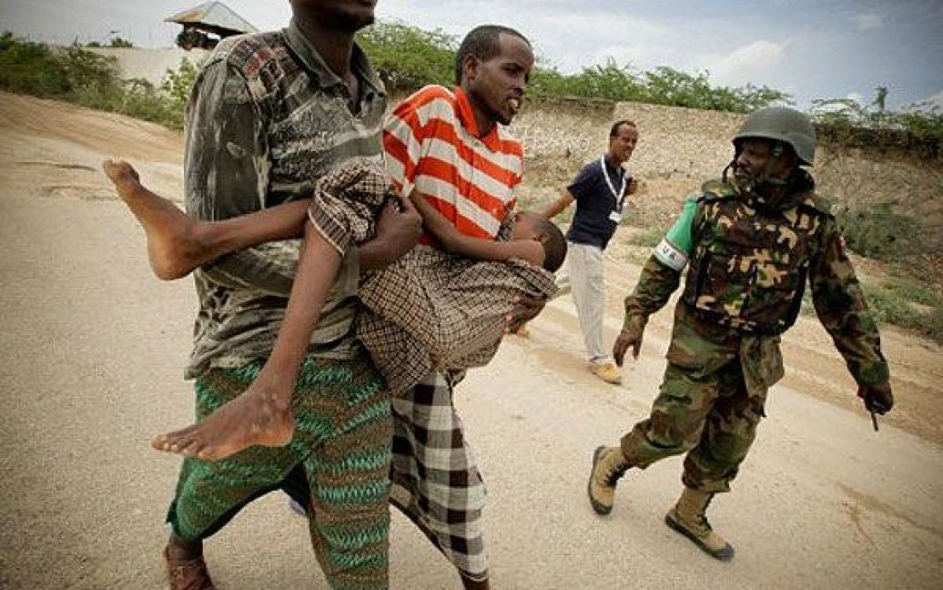 Сомалі, Могадішо. Чоловіки несуть дитину, яка страждає від важкої недостатності харчування, з табору для внутрішньо переміщених осіб в Могадішо. Штаб-квартира Місії Африканського союзу в Сомалі надала невідкладну медичну допомогу мешканцям табору, які потерпають від посухи. Фото AFP/AU-UN IST/STUART PRICE / © AFP