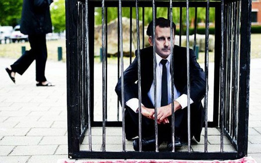 Нідерланди, Гаага. Протестувальник у масці сирійського лідера Башара аль Асада сидить на землі всередині клітки перед Міжнародним кримінальним судом в Гаазі. Делегації різних рухів із захисту прав людини вимагають дій з боку МКС щодо режиму Асада. / © AFP