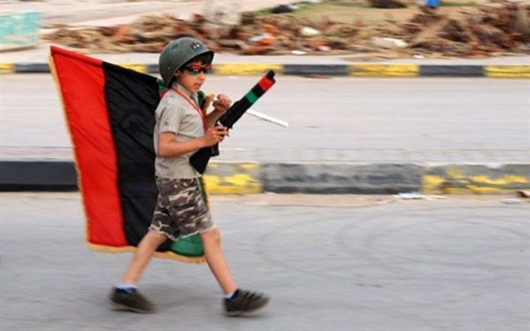 Лівійська Арабська Джамахірія, Бенгазі. Лівійська дитина, одягнена у солдатську форму, тримає прапор під час прогулянки площею Революції в повстанському місті Бенгазі. / © AFP