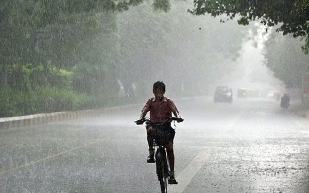 Індії Нью-Делі. Індійський школяр катається на велосипеді під час сильного дощу в Нью-Делі. Щорічні сильні зливи з червня по вересень є життєво важливими для сотень мільйонів фермерів та економічного зростання третьої за величиною економки Азії. / © AFP