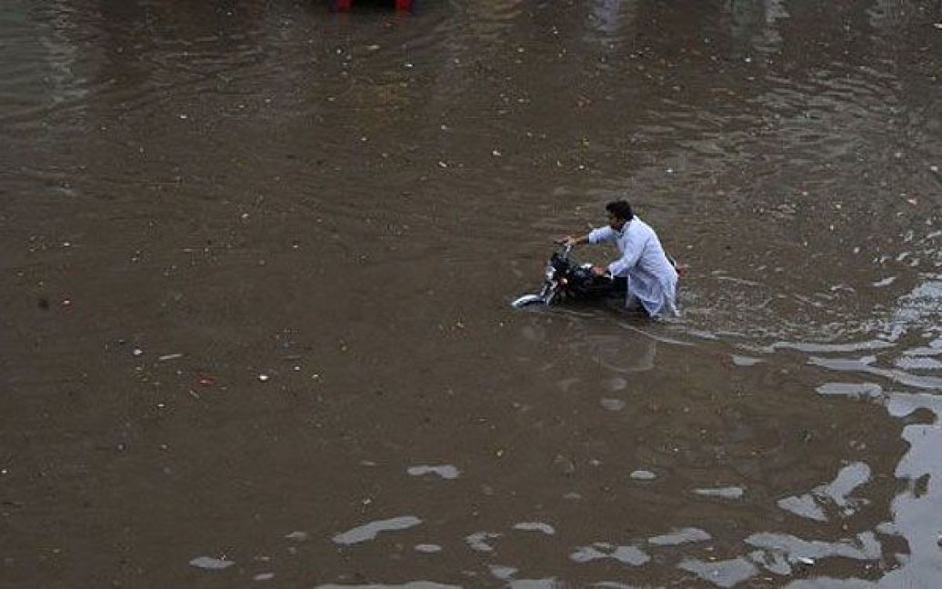 Пакистан, Лахор. Перехожий штовхає свій мотоцикл через вулицю в Лахорі, яку затопило після мусонних дощів. Повені, викликані мусонними дощами, можуть загрожувати мільйонам людей, але країна цього року краще підготувалась до стихії після масштабної кризи 2010 року. / © AFP