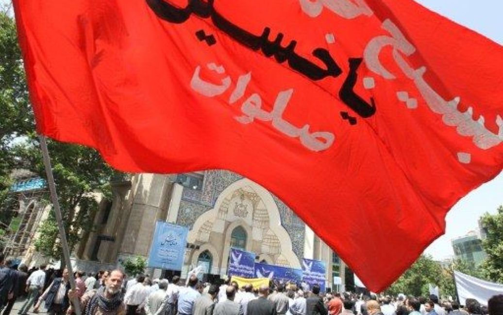 Іран, Тегеран. Іранець розмахує великим червоним прапором із зверненням до внука пророка Мухаммеда "О, Хусейн!" під час акції протесту у Тегерані. Акцію провели на підтримку шиїтського мусульманського населення Бахрейну. / © AFP