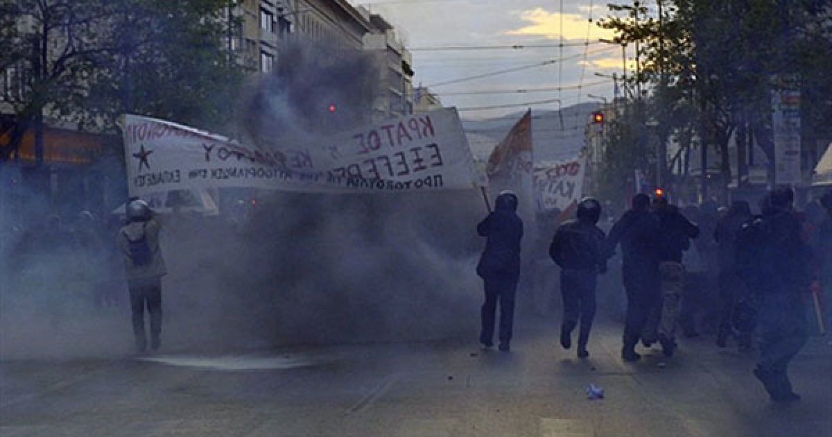 Греція, Афіни. Демонстранти тримають прапори, доки вони проходять крізь хмару сльозогінного газу під час акції протесту проти жорстокості поліції в Афінах. Четверо поліцейських були звільнені в Афінах після того, як десятки людей отримали поранення з боку поліції під час розгону акції протесту. / © AFP