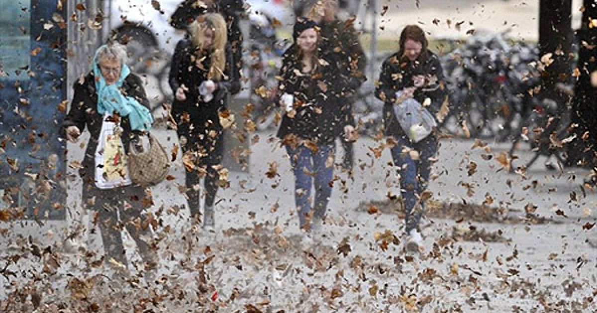 Швеція, Стокгольм. Люди йдуть вулицею серед листя, яке піднімає сильний вітер. Поривчастий вітер у Стокгольмі призвів до обриву ліній електропередачі. / © AFP