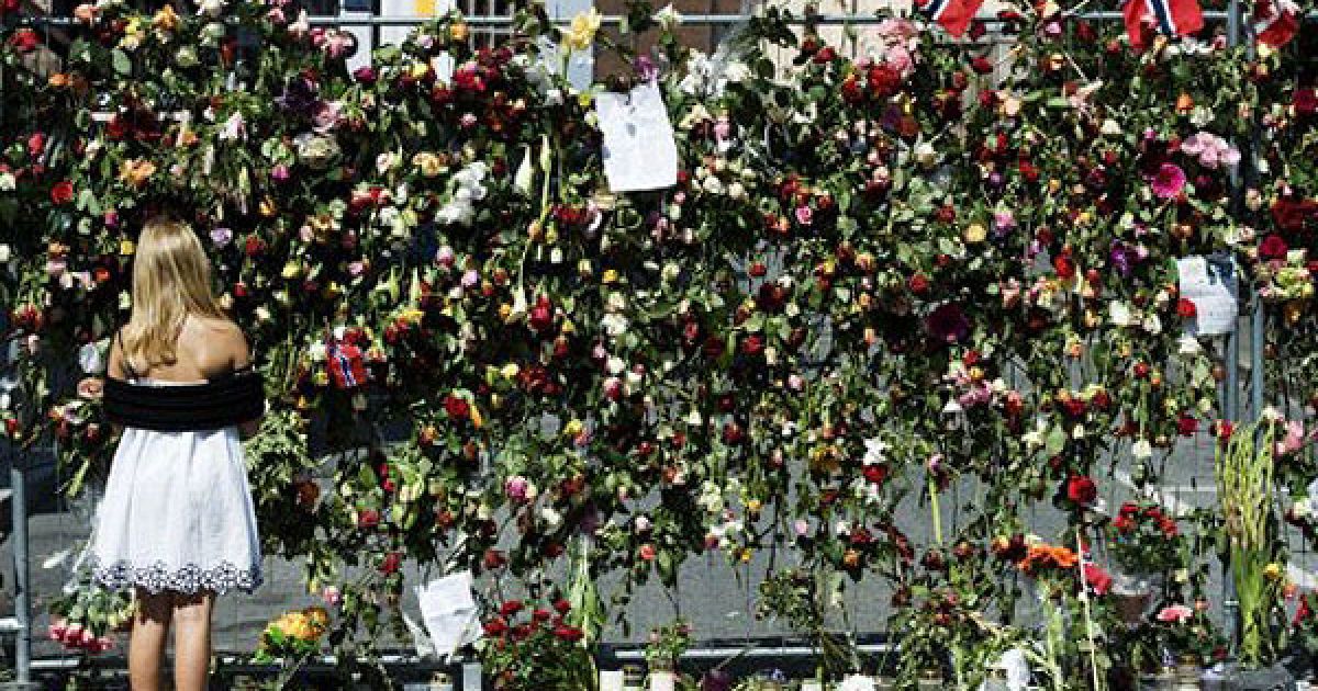 Норвегія, Осло. Дівчина дивиться на паркан безпеки, вкритий квітами, перед штаб-квартирою уряду на місці вибухів в Осло. Число людей, зниклих без вісті після масового вбивства та стрілянини на острові поблизу Осло знизилося з п&#039;яти до одного. / © AFP