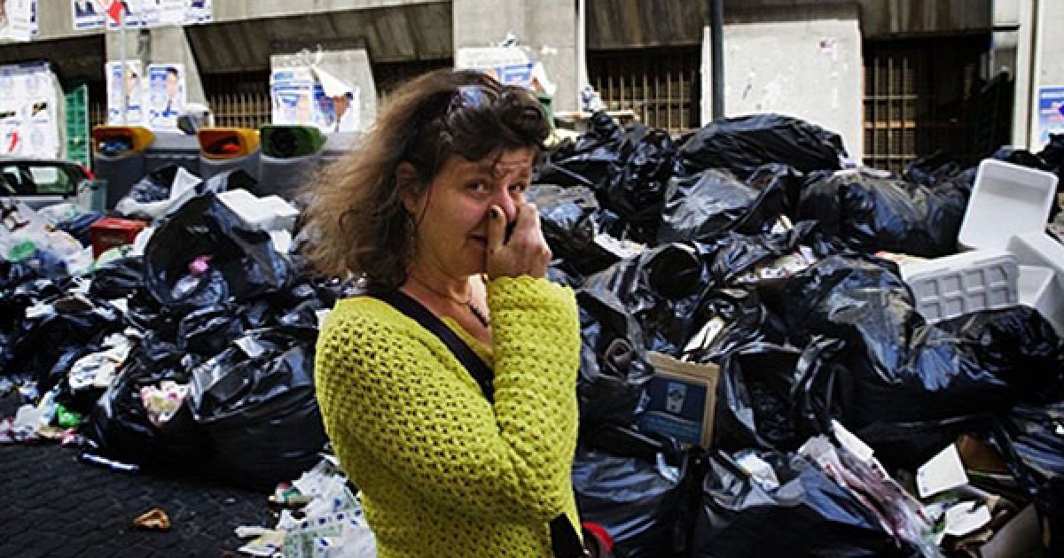 Італія, Неаполь. Жінка закриває носа, коли вона проходить повз купи сміття на вулиці в районі Поццуолі, передмісті Неаполя. Італійські солдати прибули до Неаполя, щоб почати очищення міста від сміття, якого там назбиралось більше 4 тисяч тонн. / © AFP