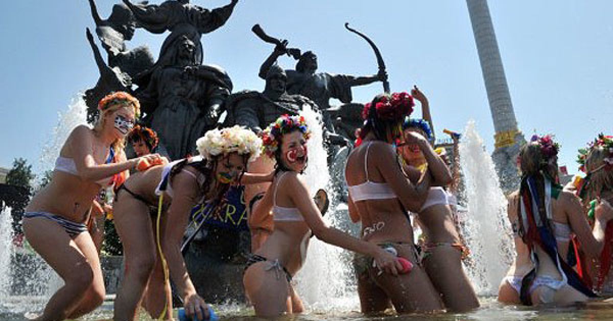 Україна, Київ. Активістки жіночого руху FEMEN, розфарбовані як міжнародні футбольні фанати, купаються у фонтані на Майдані Незалежності в Києві під час акції протесту "Євро-мийка 2012". Дівчата протестували проти щорічного літнього відключення гарячої води в українській столиці. / © AFP