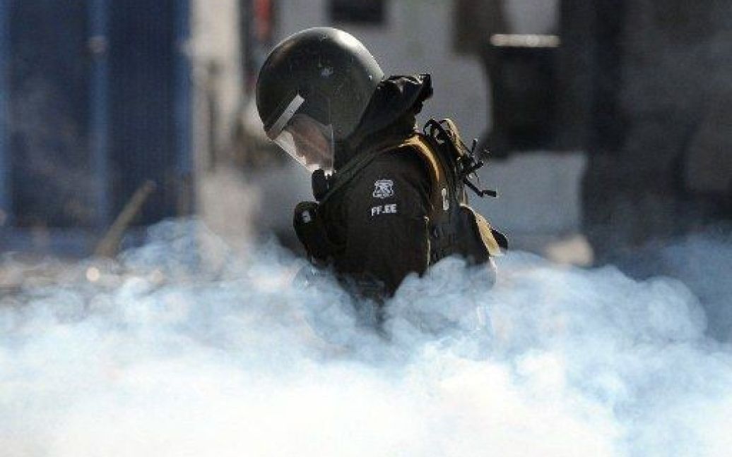 Чилі, Сантьяго. Поліцейський йде крізь хмару газу під час акції протесту в Сантьяго. Десятки людей приєдналися до святкування Дню молодих бойовиків. / © AFP