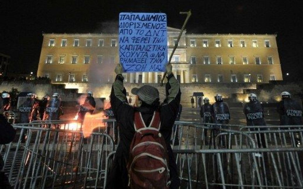 Греція, Афіни. Чоловік тримає плакат з антиурядовими закликами під час акції протесту перед парламентом в Афінах. Грецькі профспілки поновили протести. / © AFP