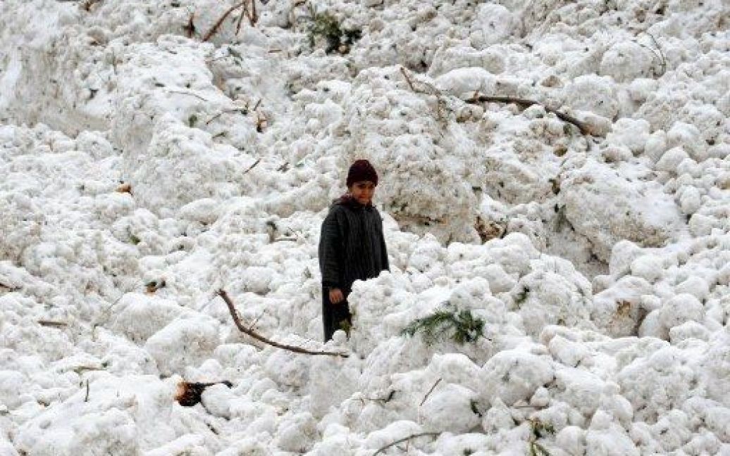 Індія, Рамварі. Хлопчик стоїть у снігу після сходу лавини на містечко Рамварі поблизу Срінагара. Щонайменше дев&#039;ять індійських військових загинули під час сходу лавини в горах Кашміру, кілька солдатів зникли безвісти. / © AFP