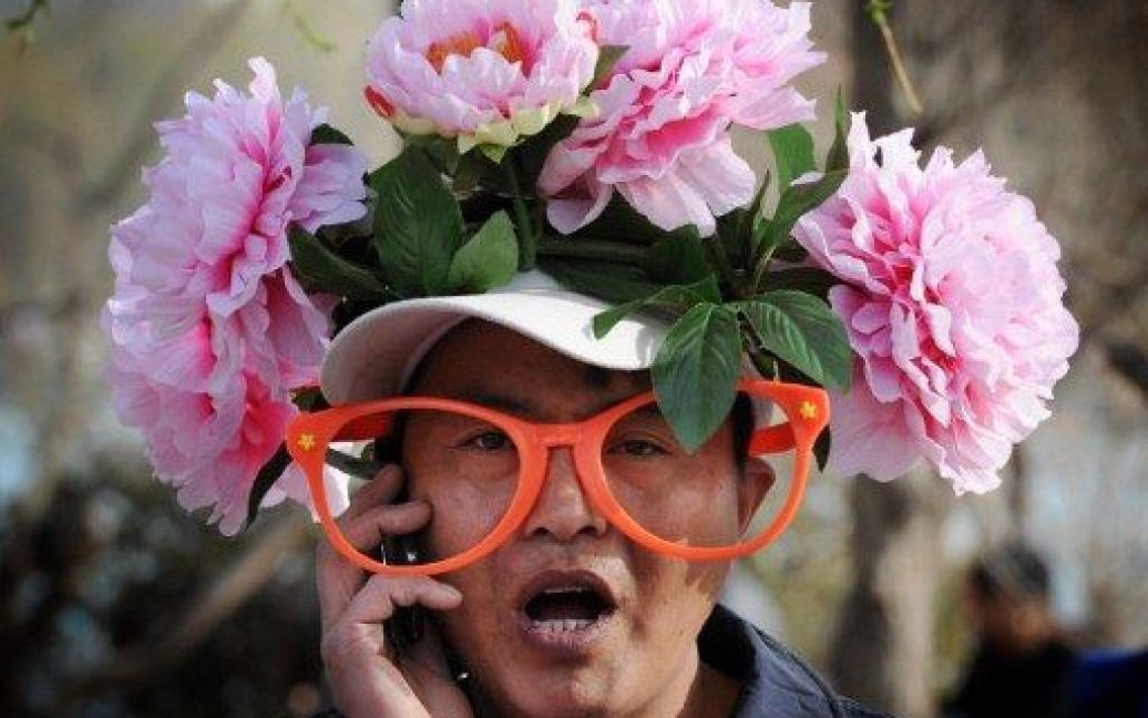 Пекін, Китай. Продавець квітів у яскравому капелюсі торгує в парку Yuyuan Tan на початку сезону цвітіння сакури в Пекіні. / © AFP