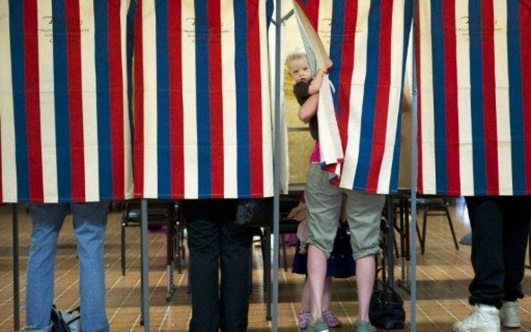 США, Пеорія. Дитина визирає з кабінки для голосування, доки його мати віддає свій голос на загальних виборах у штаті Іллінойс. / © AFP