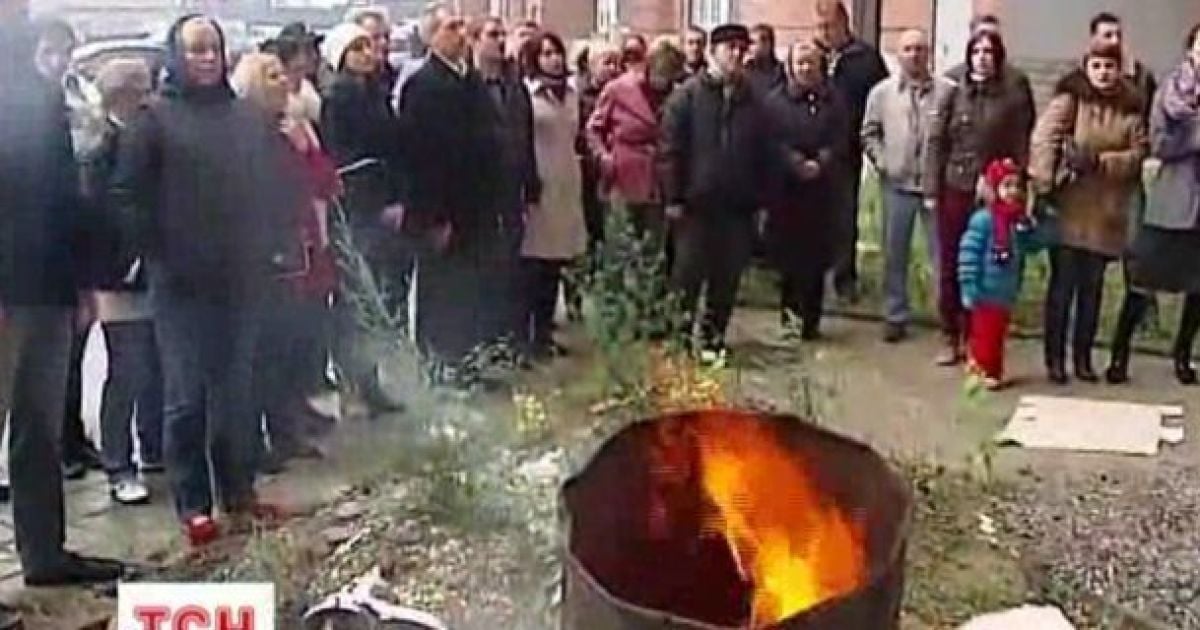 Люди гріються біля багаття, що розпалили у дворі будинку.