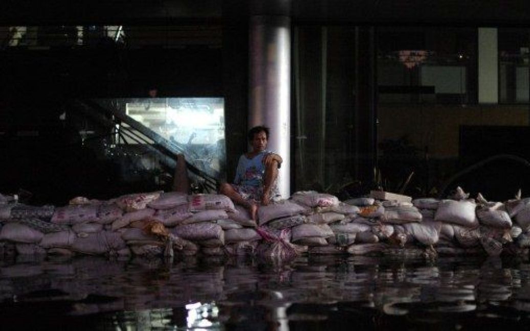 Таїланд, Бангкок. Людина сидить на мішках з піском перед будівлею уряду на затопленій вулиці в Бангкоку. Число загиблих в результаті найсильнішої за останні десятиліття повені у Таїланді перевищило 400 осіб. / © AFP