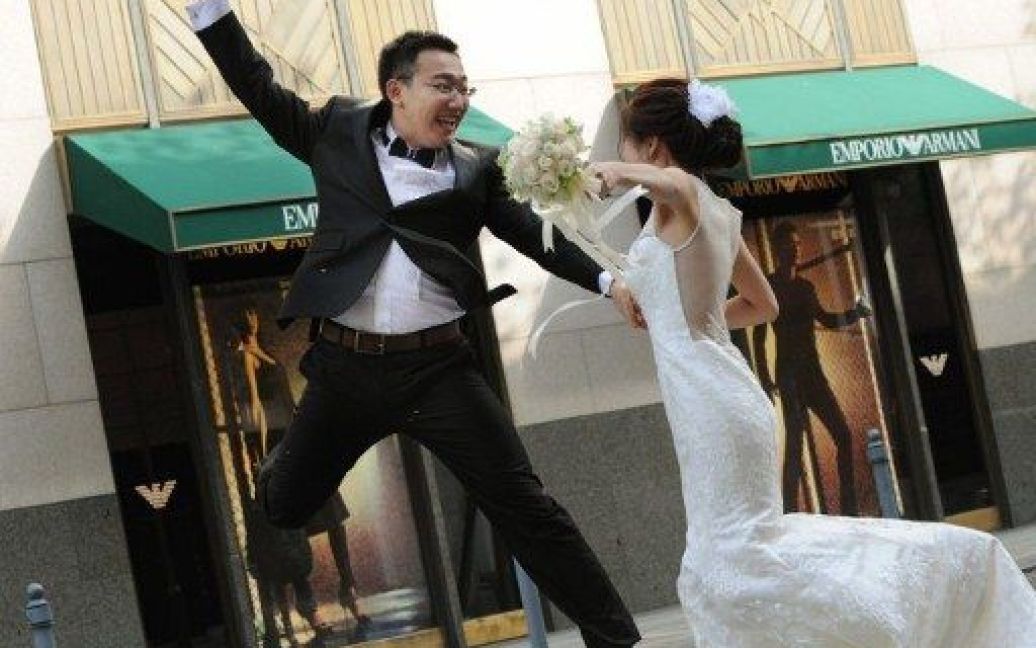 Китай, Шанхай. Наречені стрибають у повітря перед магазином одягу "Armani" в Шанхаї. На відміну від Заходу, китайські весільні фотографії, як правило, роблять за кілька місяців до весільної церемонії. Пара позує фотографу у західних та китайських костюмах. / © AFP