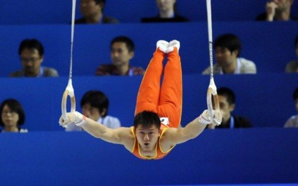 Японія, Токіо. Китайський гімнаст Чень Ібінь виконує вправу на кільцях під час командного заліку серед чоловіків у фіналі Чемпіонату світу з гімнастики. / © AFP