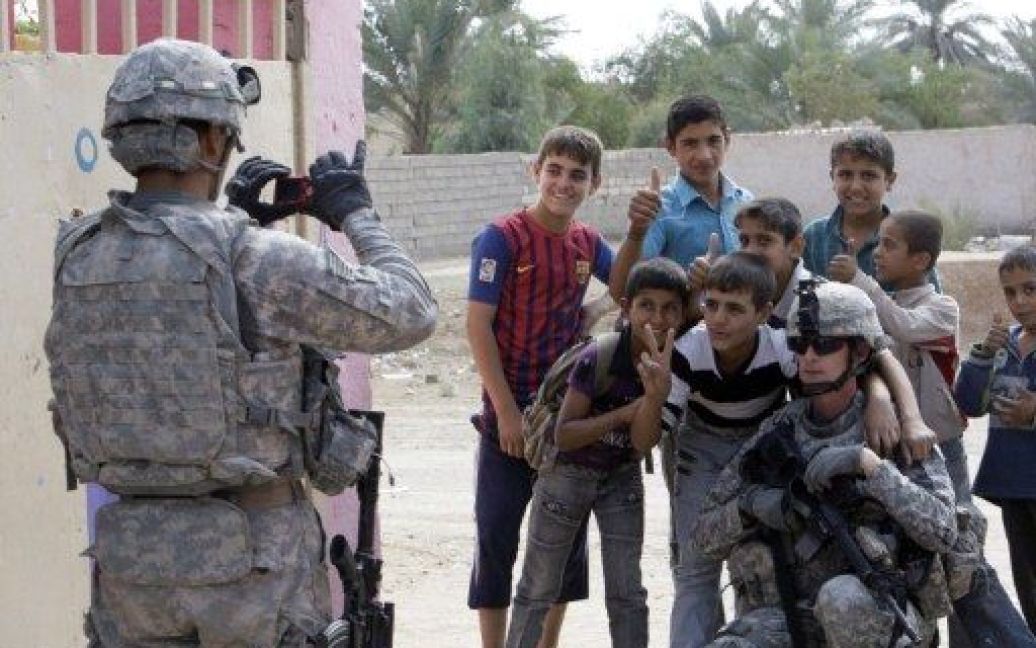 Ірак, Багдад. Американський солдат знімає свого товариша поруч з іракськими школярами у місті Іскандірія в провінції Бабельпоблизу Багдада. Американські військові пожертвували книги та подарунки місцевим учням. / © AFP