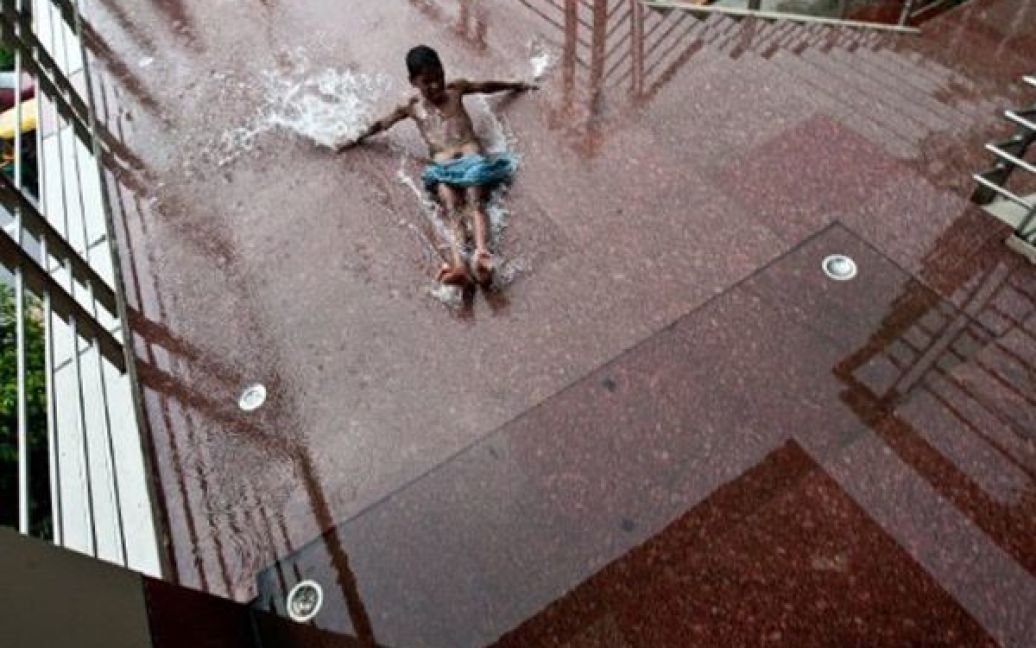 Індія, Делі. Безпритульний хлопчик бавиться на мокрих сходах одного з пішохідних мостів. В Індії розпочався сезон мусонів. / © AFP