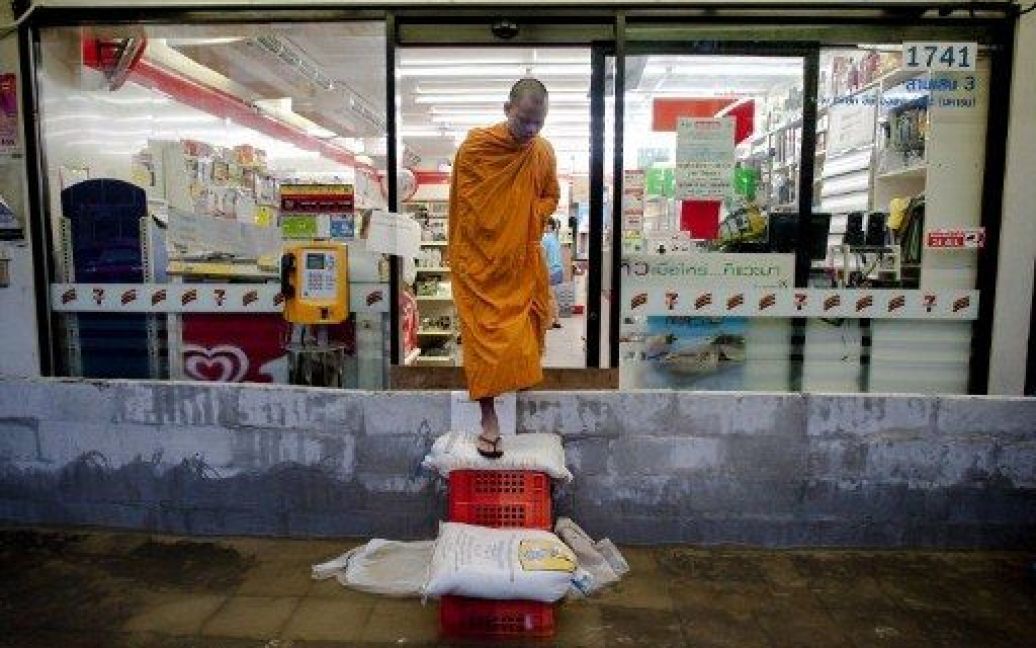 Таїланд, Бангкок. Буддійський чернець виходить з магазину, навкого якого встановлені захисні блоки з ящиків і мішків з піском для блокування повені. Прем&#039;єр-міністр Таїланду попередив мешканців Бангкоку, що повінь може тривати ще протягом чотирьох тижнів, доки рівень води впаде. / © AFP