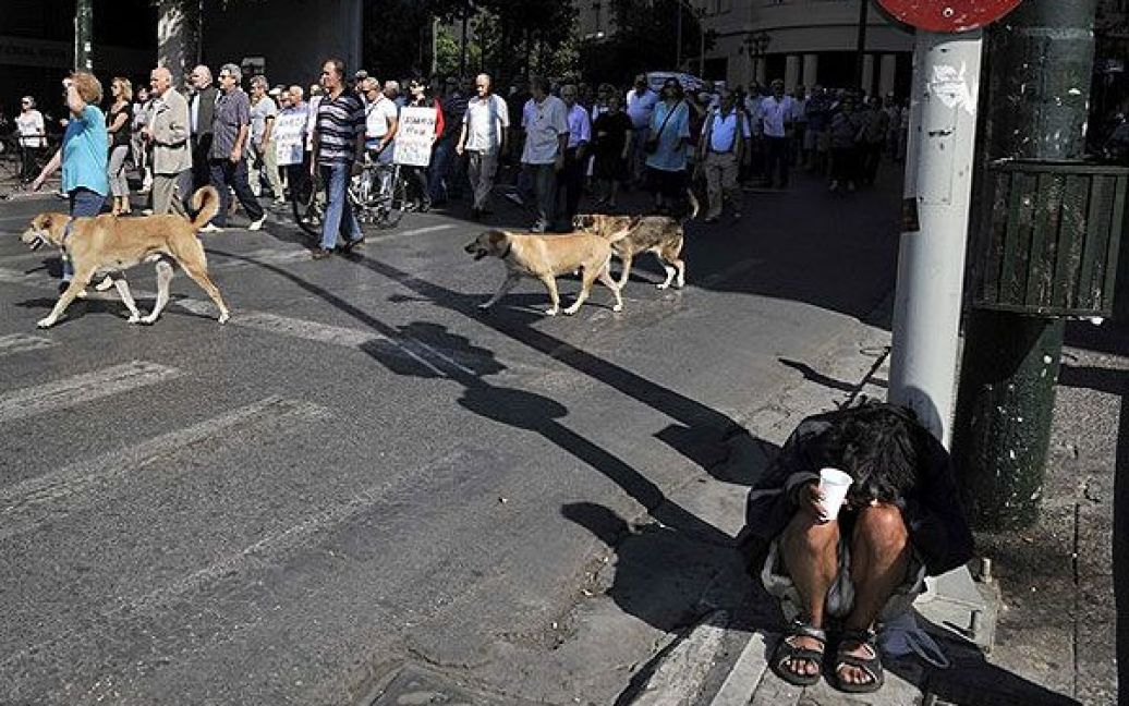 Греція, Афіни. Чоловік просить милостиню на тлі пенсіонерів, які влаштували марш протесту до Міністерства фінансів в центрі Афін. / © AFP
