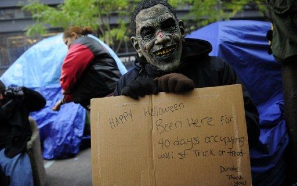 США, Нью-Йорк. Учасник акції протесту "Окупуй Уолл-стріт" в костюмі зомбі з обличчям президента США Барака Обами сидить перед своїм наметом в парку Zuccotti. / © AFP