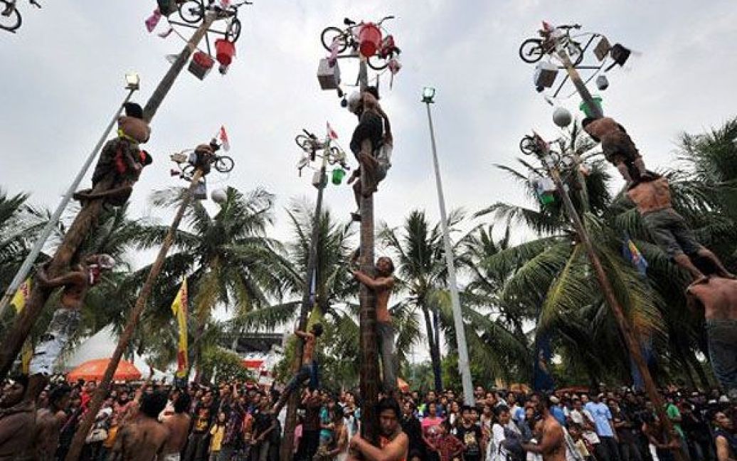 Індонезія, Джакарта. Чоловіки намагаються піднятися на змащені слизом стовпи, на верхівках яких закріплені подарунки, під час святкування Дня Незалежності в Джакарті. Індонезія відзначає 66-ту річницю визволення від голландського панування. / © AFP