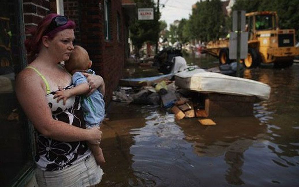 США, Воллінгтон, штат Нью-Джерсі. Жінки тримає на руках дитину, стоячи посеред вулиці, затопленої в результаті потужних злив, які приніс з собою ураган "Айрін". В результаті удару урагану "Айрін" тисячі жителів були змушені залишити свої будинки, багато залишились без електрики. / © AFP