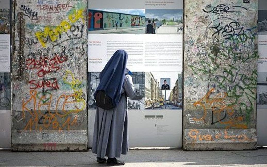Німеччина, Берлін. Черниця роздивляється малюнки на плитах-залишках Берлінської стіни, виставлених на Потсдамській площі в Берліні. Берлінська стіна колись розділяла місто протягом майже 30 років. / © AFP