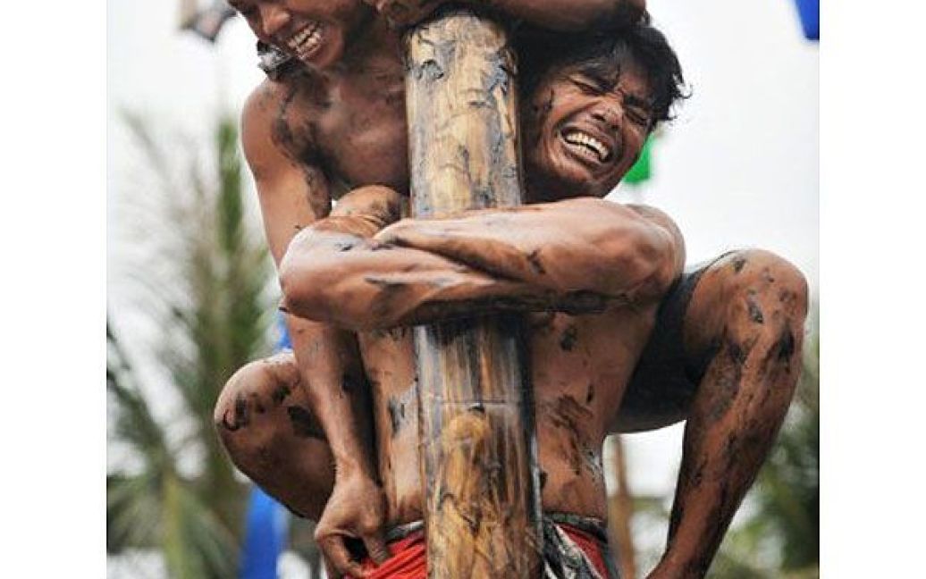 Індонезія, Джакарта. Чоловіки намагаються підійнятися на змащений і слизький стовп, на вершині якого прикріплено приз, під час святкування Дня Незалежності Індонезії у Джакарті. Індонезія відзначила 66-ту річницю визволення від голландського панування. / © AFP