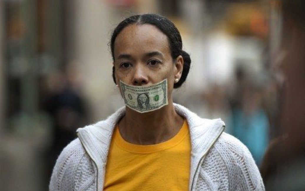 США, Нью-Йорк. Учасниця акції протесту "Окупуй Уолл-стріт" заклеїла собі рота доларовою купюрою. / © AFP