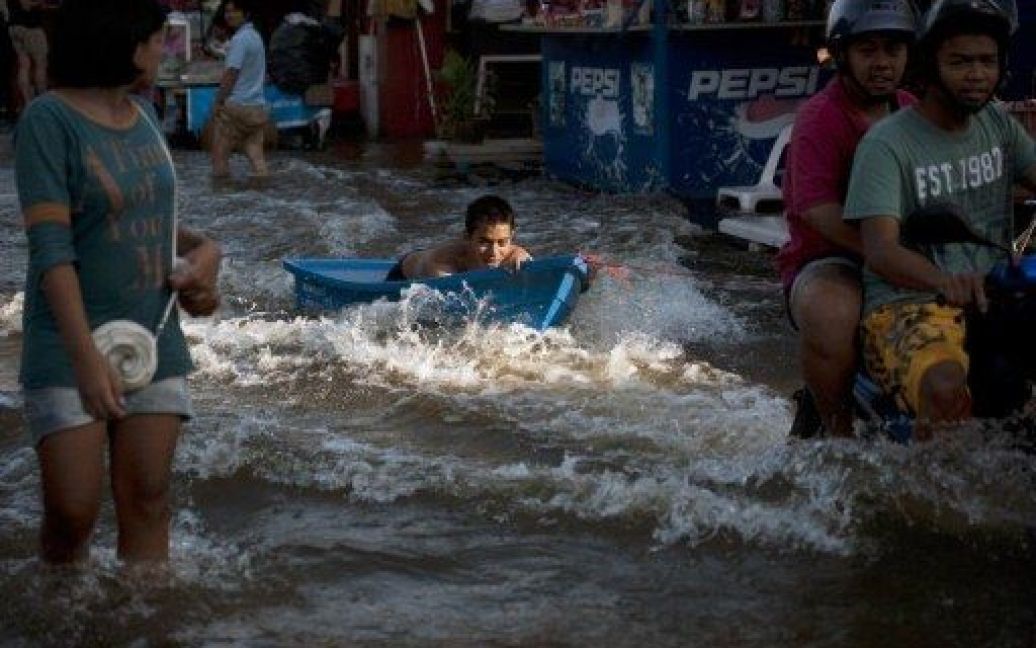 Таїланд, Бангкок. Чоловіка у невеликому пластиковому човні тягне по затопленій вулиці мотоцикл. Мільйони людей у столиці Таїланду евакуюють свої речі, оскільки місту загрожує повінь. / © AFP