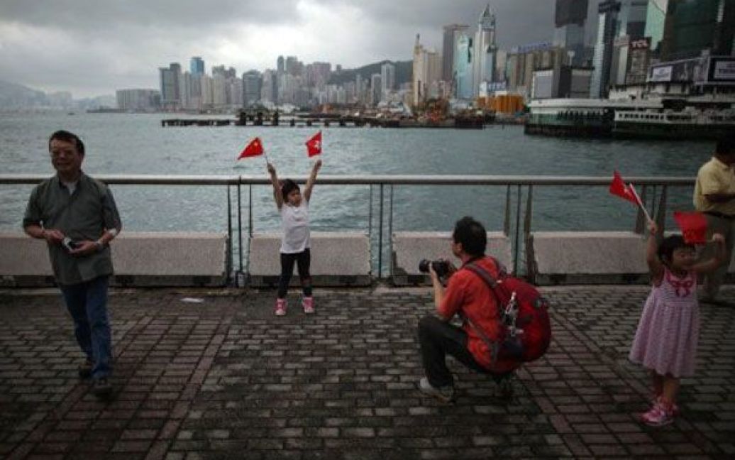 Китай, Гонконг. Дівчинка тримає прапори Гонконгу і Китаю під час фотосесії на тлі хмарочосів Гонконгу. Китай разом з Гонконгом і Макао відзначив 62-у річницю незалежності. / © AFP
