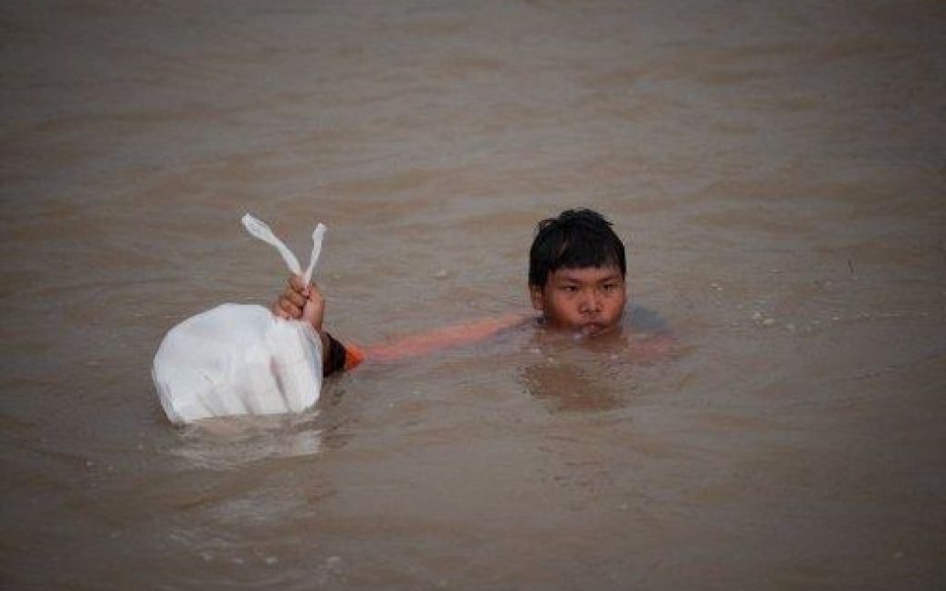 Таїланд, Аюттая. Хлопчик переносить через затоплену вулицю пакунок з продовольчою допомогою, яку військові роздають потерпілим від потужної повені. / © AFP