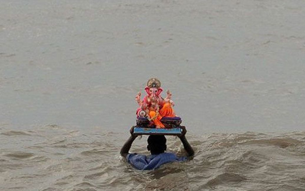 Індія, Мумбаї. Індус із фігурою індуїстського бога Ганеша занурюється у воду під час святкування десятиденного фестивалю "Ганеш Чатурті" в Мумбаї. / © AFP