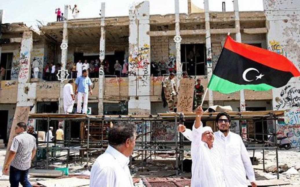 Лівійська Арабська Джамахірія, Тріполі. Лівієць розмахує повстанським прапором, коли мешканці Тріполі відвідують знищену колишню резиденцію Каддафі "Баб Аль-Азізія". Повстанські сили приготувались до можливих атак з боку залишків прихильників Муаммара Каддафі. / © AFP