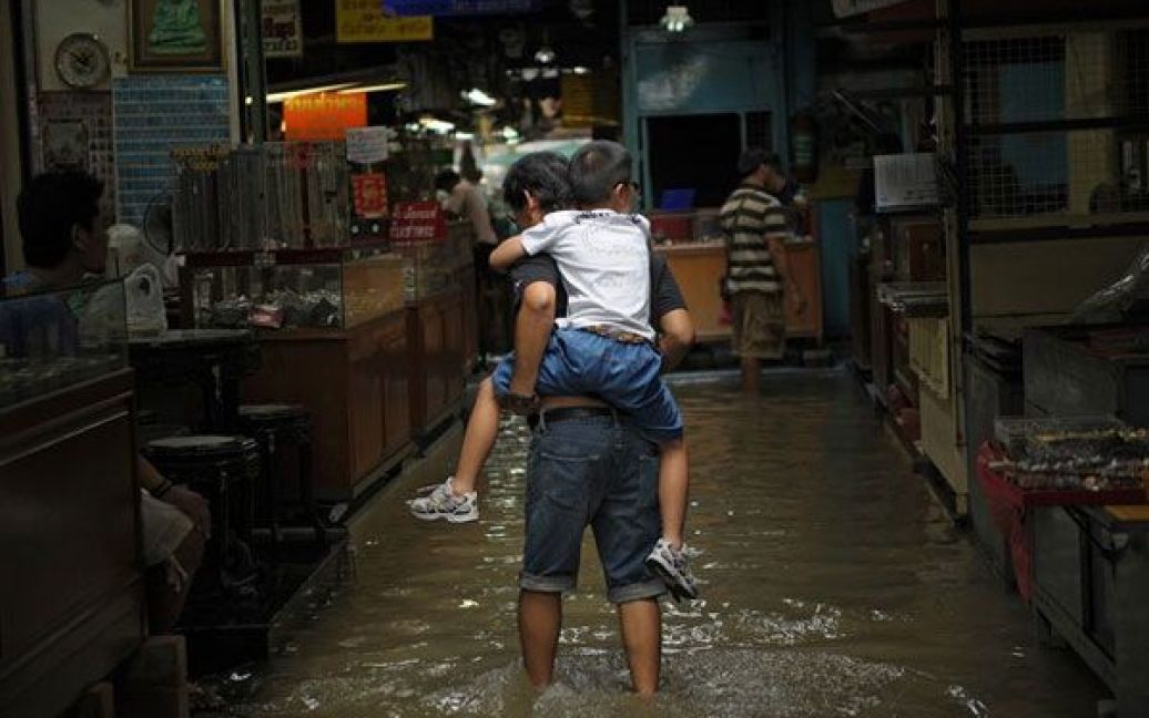 Таїланд, Бангкок. Чоловік несе хлопчика на спині через затоплений ринок у місті Бангкок. В результаті найгірших за останні десятиліття мусонних повеней, в Таїланді загинули 224 людини, постраждало від повеней три чверті населення країни. / © AFP