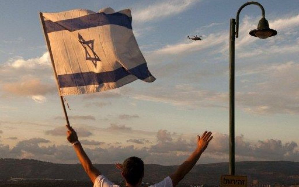 Ізраїль, Міцпе Хіла. Ізраїльтяни розмахують прапорами, вітаючи вертоліт, на якому до свого рідного міста прибув ізраїльський капрал Гілад Шаліт пілся 1940 днів у палестинському полоні. Гілада після п&#039;яти років ув&#039;язнення обміняли на тисячу палестинських ув&rsquo;язнених. / © AFP