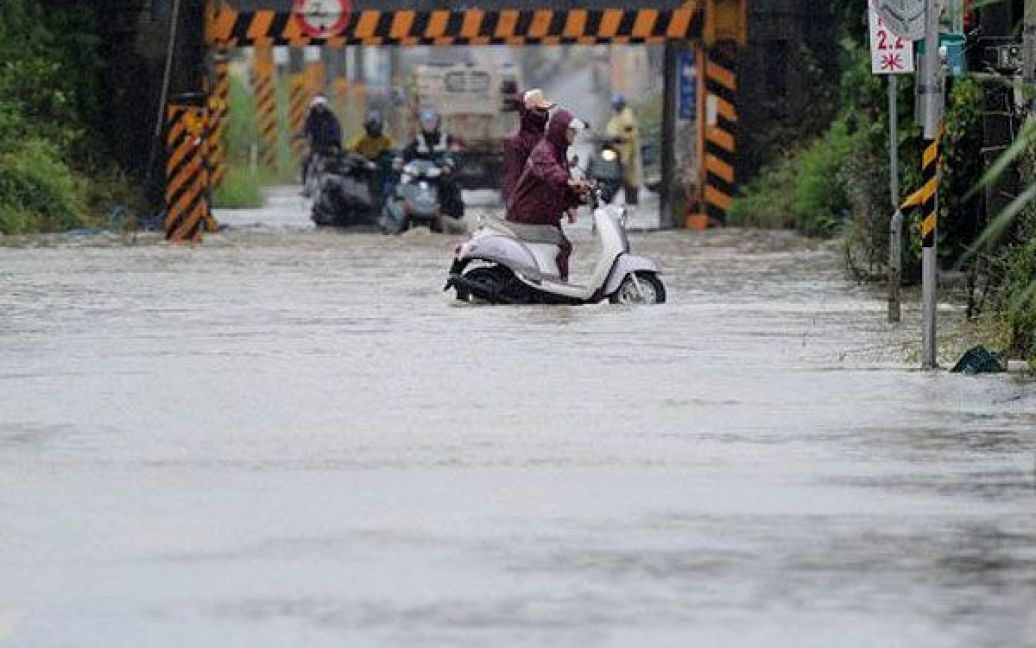 Тайвань, Піндун. Місцеві мотоциклісти намагаються провезти свої мотоцикли через вулицю, затоплену під час повені, викликаної тайфуном Нанмадол на півдні Тайваню. Тисячі людей були евакуйовані, школи закриті, припинено залізничний рух, коли тайфун прокотився найбільш густонаселеними районами країни. / © AFP