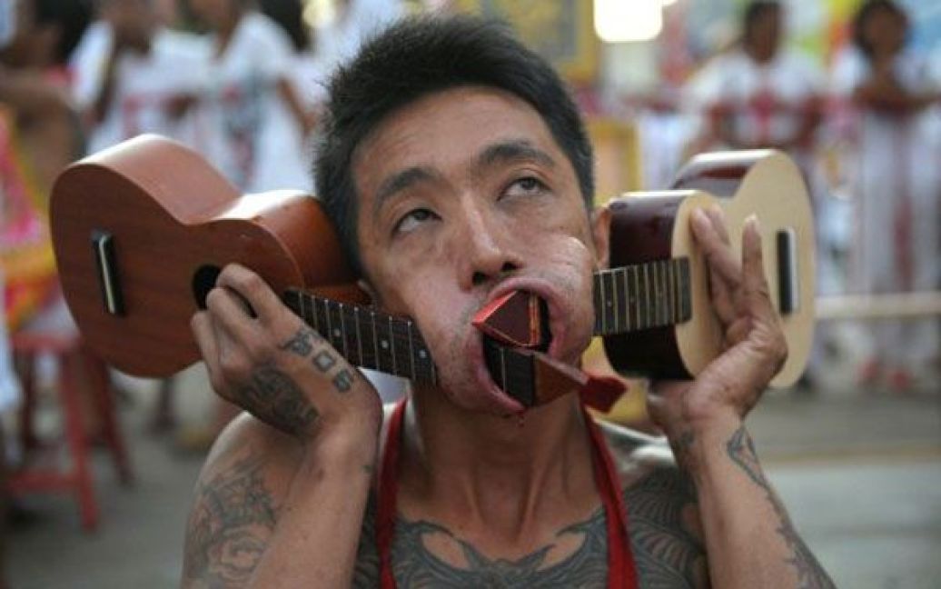 Таїланд, Пхукет. Віруючий із щоками, в які вставлено дві маленькі гітари, бере участь у вуличній ході з нагоди щорічного Вегетаріанський фестивалю в Пхукеті. Під час фестивалю, який триває дев&#039;ять днів, віруючі проколюють собі щоки гострими предметами, вчиняють інші болючі дії, щоб очистити себе. / © AFP