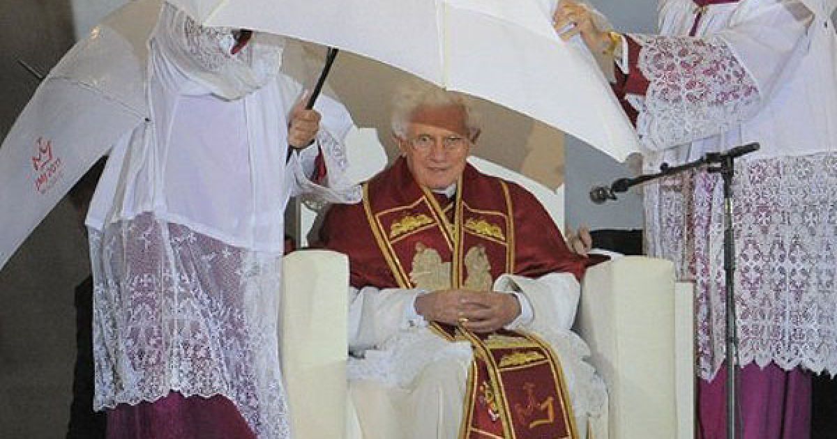 Іспанія, Мадрид. Священики прикривають Папу Римського Бенедикта XVI парасолькою під час зливи на авіабазі Cuatro Vientos (Чотири вітри) у Мадриді. Понтифік провів на авіабазі "Молитву бдіння" на честь святкування Всесвітнього дня молоді. Близько мільйона молодих паломників вітали Папу Римського у Мадриді. / © AFP