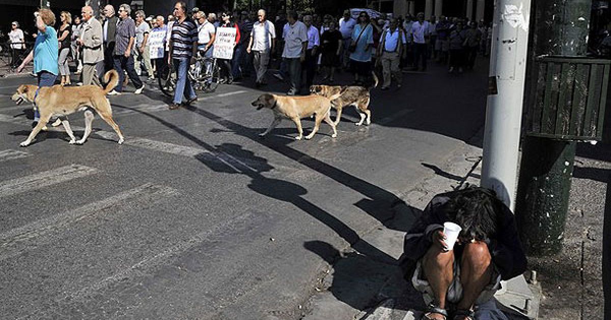 Греція, Афіни. Чоловік просить милостиню на тлі пенсіонерів, які влаштували марш протесту до Міністерства фінансів в центрі Афін. / © AFP