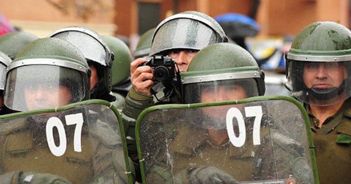 Чилі, Сантьяго. Чилійський офіцер ОМОНу фотографує студентів, які беруть участь в акції протесту проти реформ освіти та останнього урядового плану з врегулювання кризи. Тисячі чилійських студентів протягом трьох місяців протестують проти високих цін і розриву між багатими і бідними. / © AFP