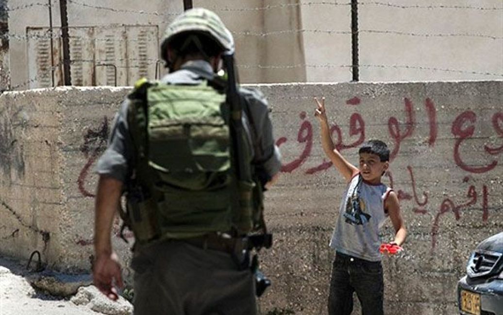Єрусалим. Палестинський хлопчик демонструє "V" (знак перемоги) ізраїльському прикордоннику, який здійснює патрулювання у районі Сільван. Ізраїльський парламентський комітет із захисту прав дітей відвідав кілька будинків з перевіркою в цьому районі. / © AFP