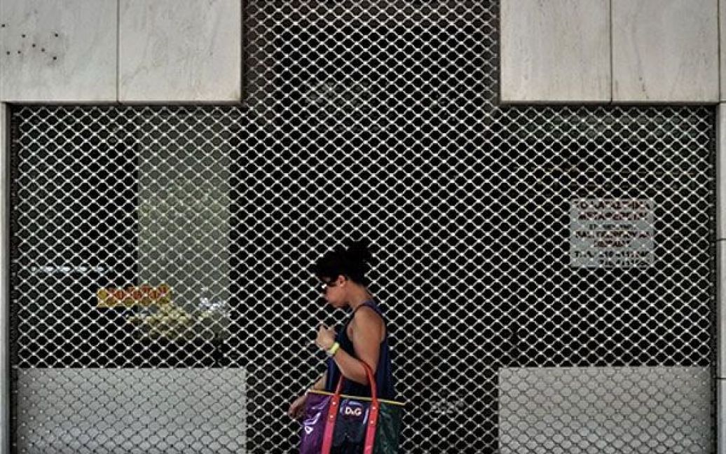 Греція, Афіни. Жінка проходить повз зачинений магазин ювелірних виробів у центрі Афін. Боргова криза і подальший економічний спад у Греції призвели до закриття майже 15 відсотків підприємств у Афінах. / © AFP
