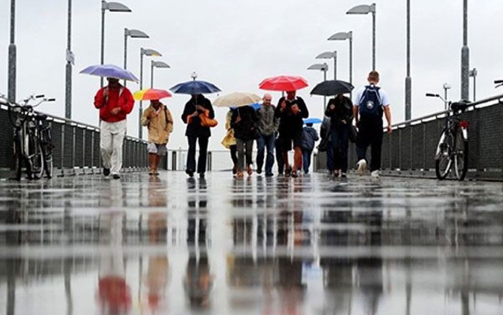 Німеччина, Берлін. Люди з парасольками гуляють під дощем на мосту в Берліні. Після тривалого періоду сонячної і спекотної погоди, температура у місті впала, небо щільно затягнуте хмарами. / © AFP