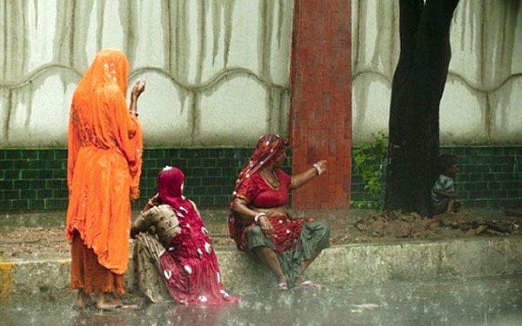 Індія, Нью-Делі. Індійські жінки сидять на узбіччі дороги, а маленький хлопчик ховається від сильного дощу. В Індії настав час мусонів, проливні дощі обрушились на кілька районів Нью-Делі і спричинили повені та ускладнення для транспорту. / © AFP